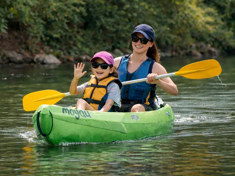 Una madre remando y una niña saludando mientras navegan por el río Sella