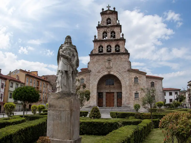 La estatua de Don Pelayo con la mano en la espada, frente a la Iglesia de la Asunción con su original campanario