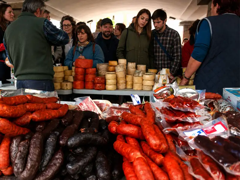 Puesto de venta de embutidos y quesos asturianos con gente en el mercado dominical de Cangas de Onís