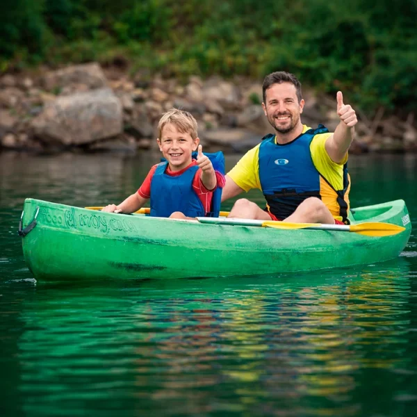 Una familia de un padre y niño pequeño sonriendo y remando en el río Sella con chalecos salvavidas.